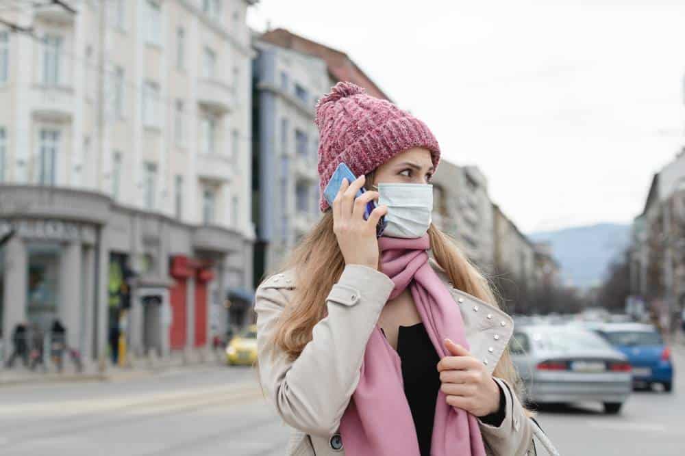 Concerned woman using her phone wearing medical mask and gloves in city